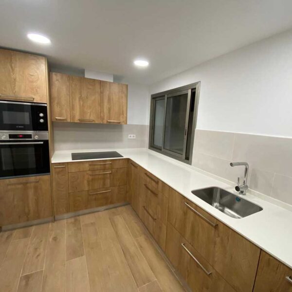 Cocina reformada con muebles de madera, encimera blanca y electrodomésticos integrados