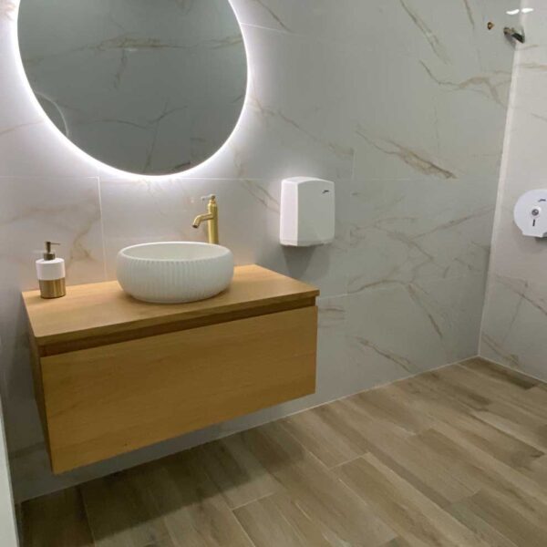 Lavabo sobre mueble de madera con espejo retroiluminado en baño reformado