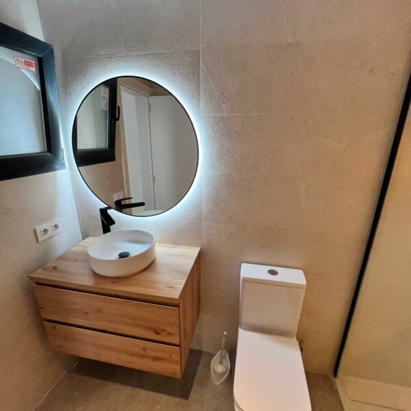 Lavabo sobre mueble de madera con espejo retroiluminado en baño reformado