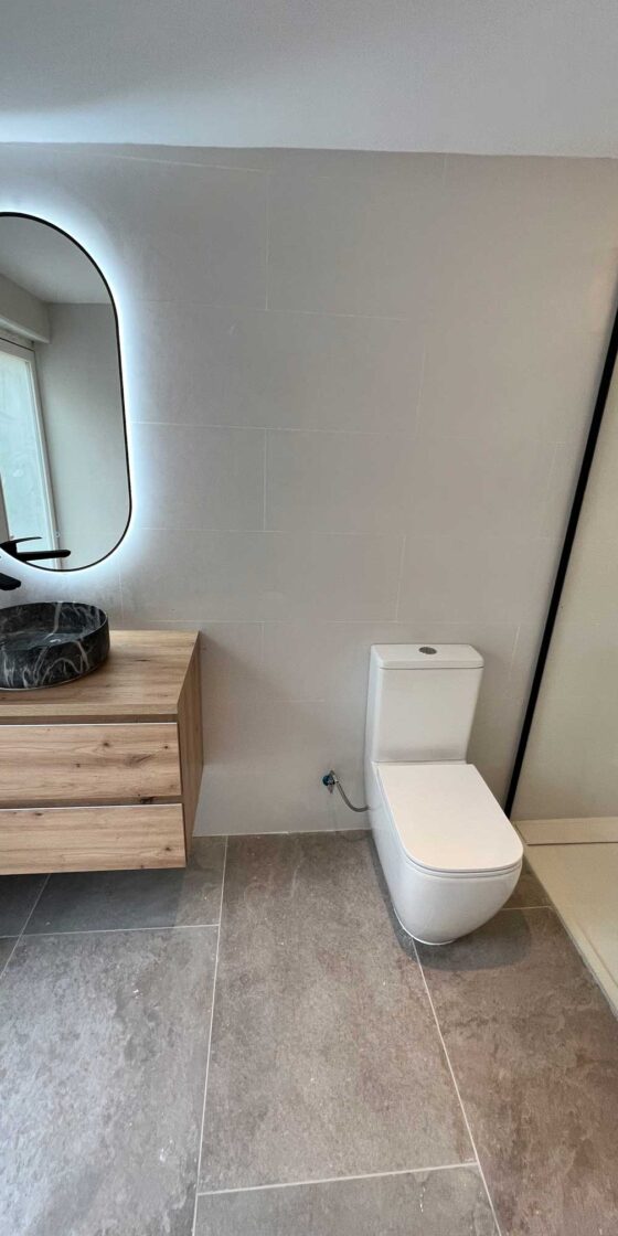 Mueble de baño suspendido con lavabo oscuro y espejo ovalado con luz LED