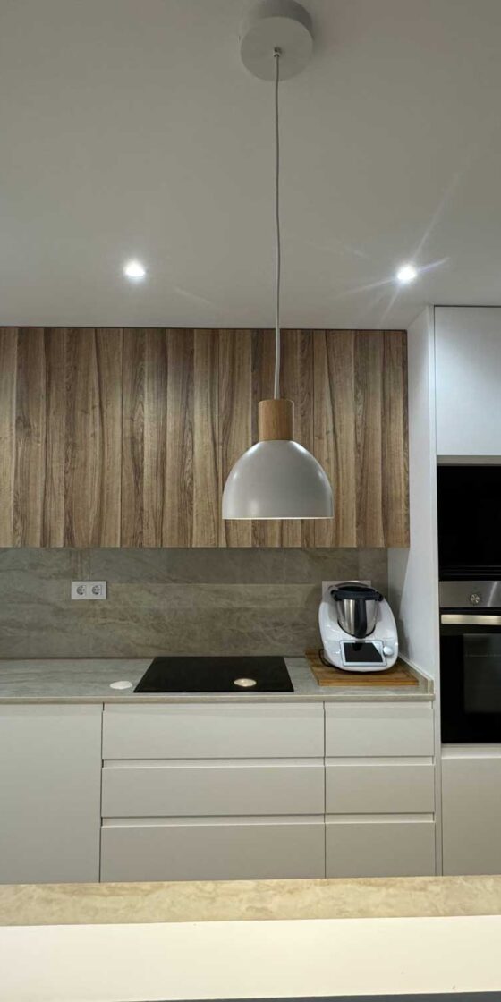 Cocina moderna con muebles blancos, panel de madera y encimera continua