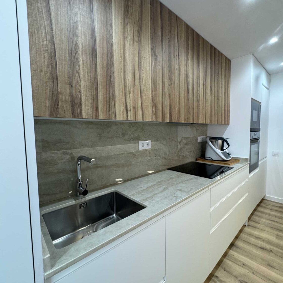 Cocina lineal con muebles blancos, armarios en madera y encimera gris