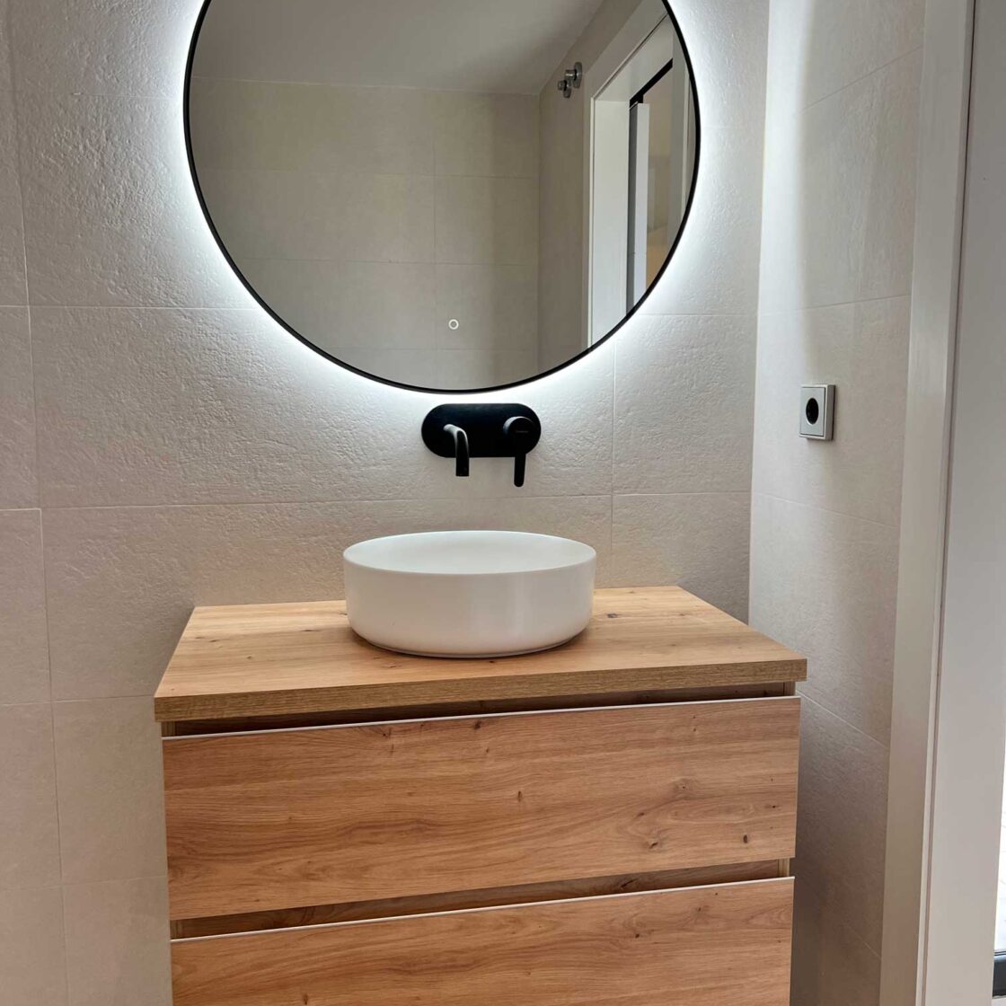 Lavabo sobre mueble de madera con espejo retroiluminado en baño reformado