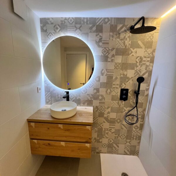 Lavabo sobre mueble de madera con espejo retroiluminado en baño reformado