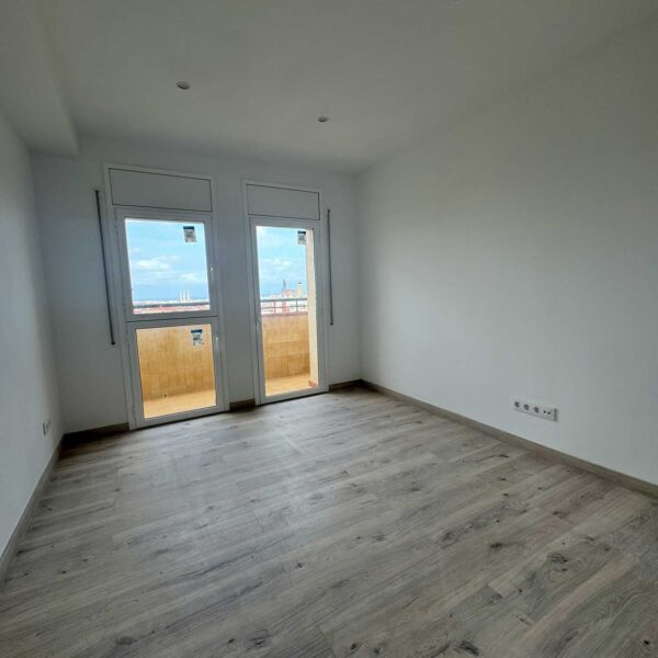 Salón vacío reformado con suelo laminado y acceso a balcón