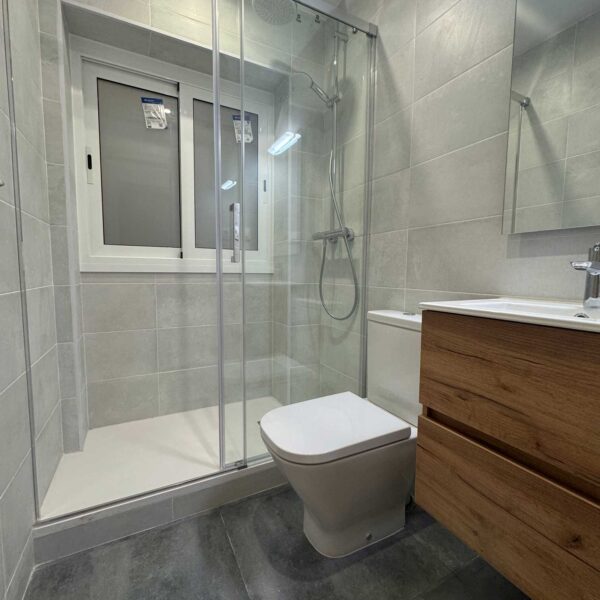 Baño moderno con plato de ducha, mampara de cristal y mueble de madera