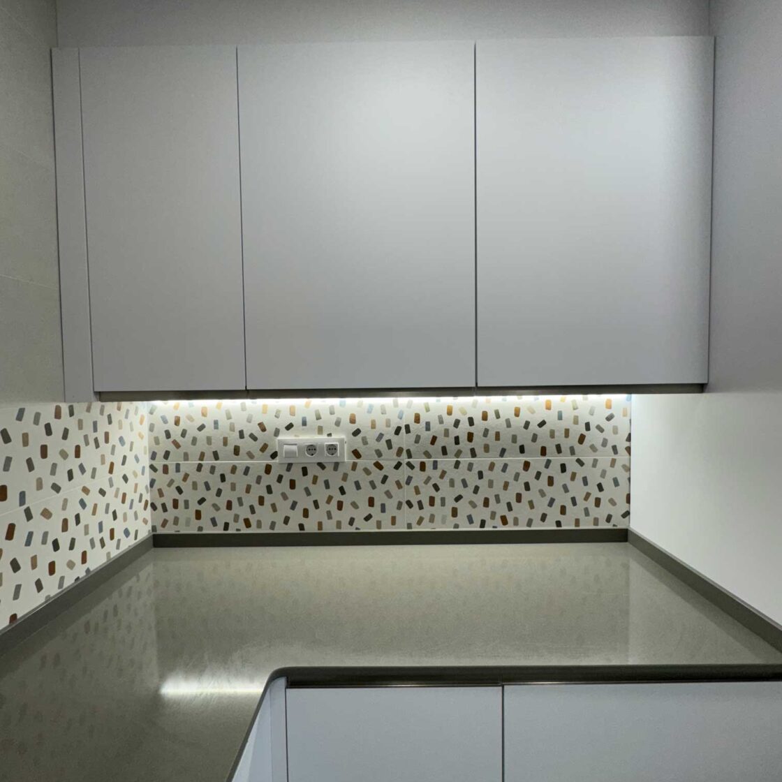 Detalle de cocina blanca con iluminación LED y encimera gris