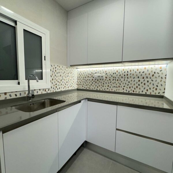Cocina en L blanca con encimera gris y salpicadero decorativo tipo mosaico